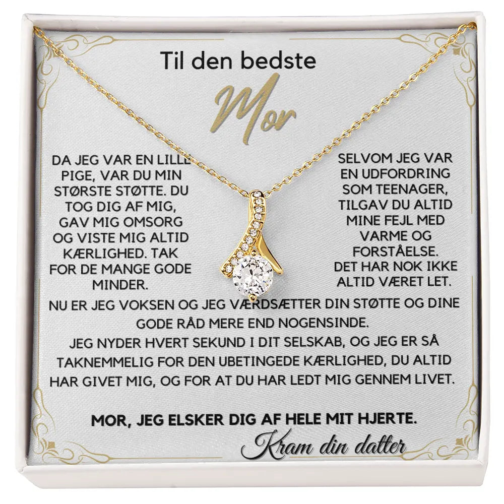 Alluring Beauty halskæde belagt med 18 karat guld i elegant sløjfe-design, med en funklende Cubic Zirkonia-sten. Leveres i gaveæske med rørende Mors Dags-kort – en personlig gave fra datter til mor.